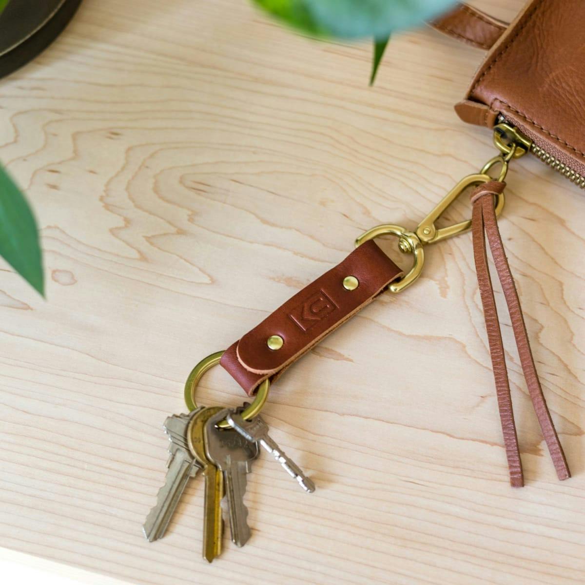 Brown leather key ring with brass metal loops and rivets on wood table.